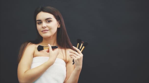 Menina bonita jovem de pé sobre um fundo preto. Ao mesmo tempo, o pincel está sorrindo em seu rosto . — Vídeo de Stock