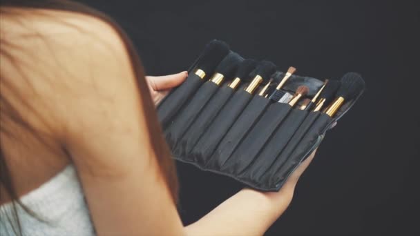 Joven chica bonita sostiene un conjunto de pinceles para el maquillaje. Conjunto de maquillaje de pincel en una caja de cuero negro que la chica sostiene en sus manos eligiendo la correcta . — Vídeos de Stock