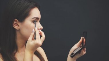 Genç bir kızın güzel yüzünün yakın çekim bir makyaj olsun. Kaşlarında fırçayla göz farı uygulayan kadın. Güzel kız aynaya bakıyor.