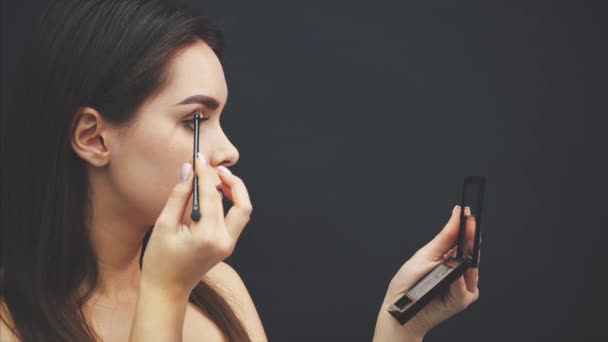 Close-up of a beautiful face of a young girl get a makeover. Woman applying an eye shadow on her eyebrows by brush. Beautiful girl looking at the mirror. — Stock Video