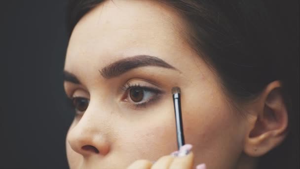 Cerrar la hermosa cara de la joven para obtener el maquillaje. Mujer aplicando sombra de ojos en sus cejas con un cepillo . — Vídeos de Stock