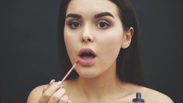 El concepto de la belleza de una mujer de moda con el pelo largo y hermoso oscuro. Mirando a la cámara y pintando los labios con lápices de labios. Retrato de primer plano de modelo con rosas rosadas, estudio con — Vídeos de Stock