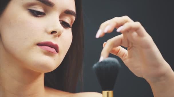 A young woman pushes a brush with his hand. The skin flies over a black background. Cropped image. Makeup application in close-up. Isolated on a black background. — Stock Video