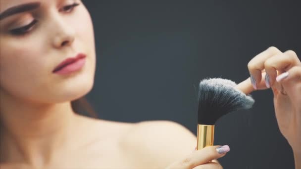 A young woman pushes a brush with his hand. The skin flies over a black background. Cropped image. Makeup application in close-up. Isolated on a black background. — Stock Video