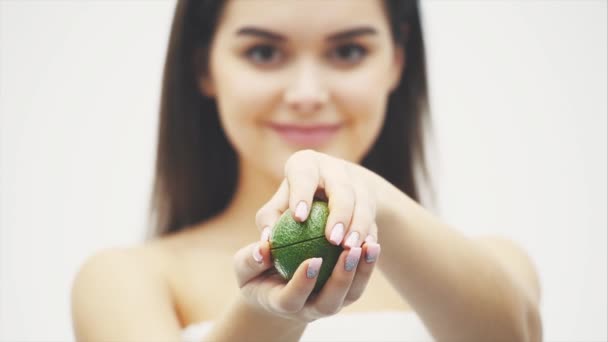 Young attractive girl stands in a studio on a black background. During this, looking into the camera holding an avocado in his hands on a blurry background opens it. — Stock Video