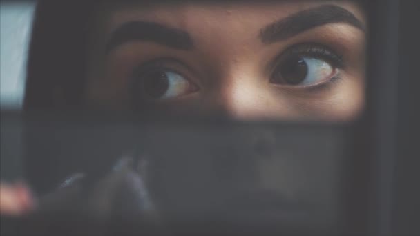 Close-up van het gezicht van een jonge vrouw krijgen een make-up. Een mooie vrouw die een oogschaduw op haar wenkbrauwen aanbrengt, is een borstel. Mooi meisje op zoek in de spiegel voor schaduwen. Close-up. — Stockvideo