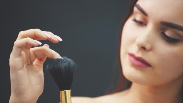 Una joven empuja un cepillo con su mano. La piel vuela sobre un fondo negro. Imagen recortada. Aplicación de maquillaje en primer plano. Aislado sobre un fondo negro. La chica tiene la piel limpia y hermosa — Vídeo de stock