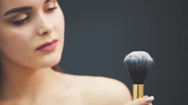 A young woman pushes a brush with his hand. The skin flies over a black background. Cropped image. Makeup application in close-up. Isolated on a black background. The girl has clean skin and beautiful — Stock Video