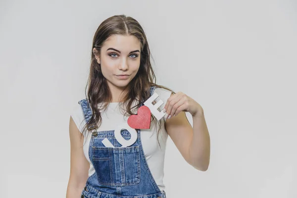 Retrato horizontal de uma mulher bonita com uma expressão confusa, encontra uma solução, vestindo um macacão de ganga casual. Isolado em um fundo cinza . — Fotografia de Stock