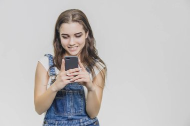 Mavi kot takım elbise ve beyaz bir t-shirt güzel genç güzel kız. Telefonu elinde tut ve ona bak. Bu içtenlikle gülümsüyor sırasında.