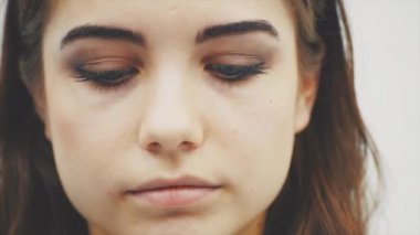 Uzun dalgalı saçlı güzel genç kadın sonra büyük mavi gözleri ile kameraya bakıyor ve kaşını yükselterek aşağı bakıyor.