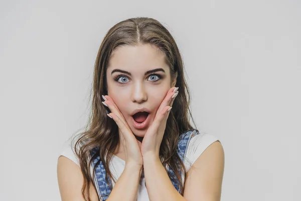 Retrato horizontal de mulher bonita com expressão confusa, encontra solução, veste camiseta casual com macacão jeans, isolado sobre fundo branco. Adorável linda estudante pensa interior — Fotografia de Stock