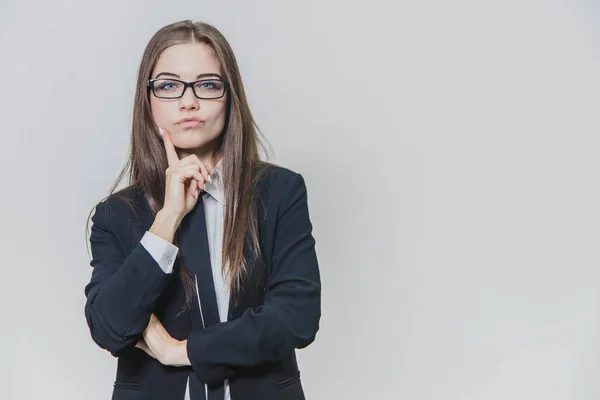 Jeune belle femme d'affaires pense avec sa main sur le menton. Curieux fille porte des lunettes avec une jante arrière et une cravate bleue . — Photo