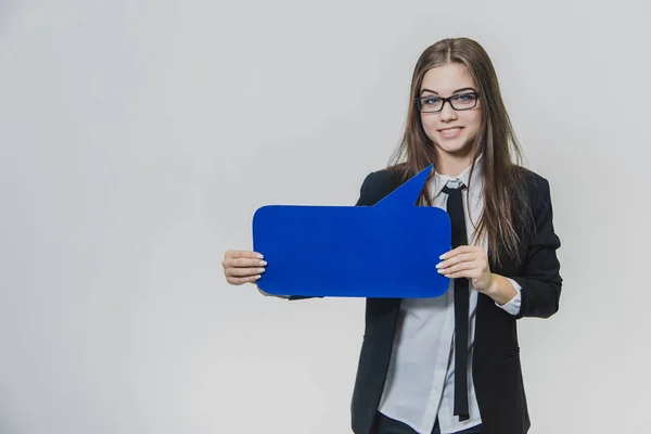 Young woman is holding a blue speech bubble in front of herself, which is rectangular-shaped, with one hand, isolated, on the white background. Young lady is looking at the camera smiling sincerely. — Stock Photo, Image