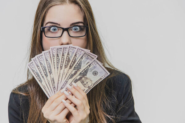 Happy excited young business woman is showing a pile of money, isolated on white background. Girl is satisfied by huge amound of bucks.