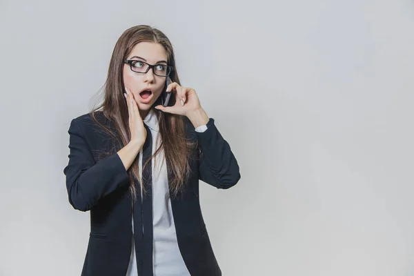 Chockad ganska affärskvinna håller en telefon i handen och pratar. Attraktiv dam ser fantastisk. Flickan vidrör hennes ansikte med höger hand. — Stockfoto