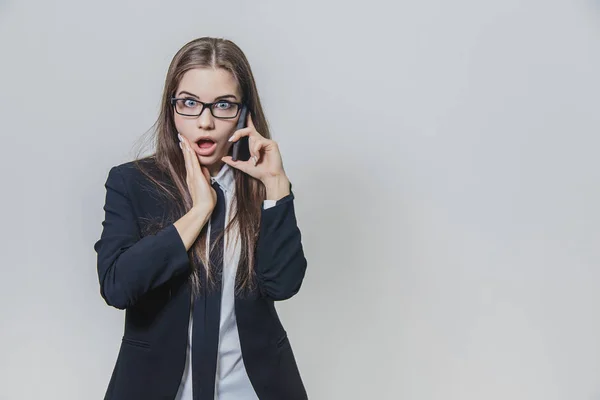 Chockad ganska affärskvinna håller en telefon i handen och pratar. Attraktiv dam ser fantastisk. Flickan vidrör hennes ansikte med höger hand. — Stockfoto