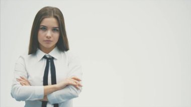 Genç güzel iş kızı beyaz bir arka plan üzerinde duruyor. Bu süre zarfında elini koluna koyar ve kameraya bakar..