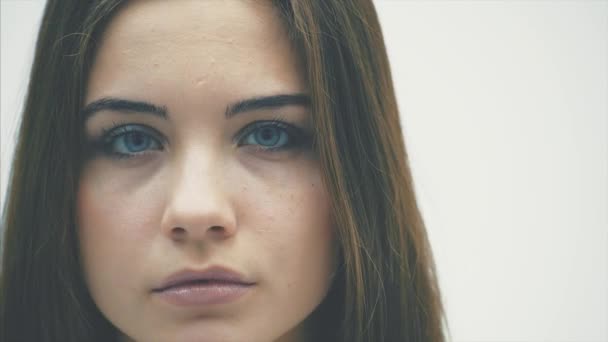 Νεαρό κορίτσι που στέκεται σε λευκό φόντο. Κατά τη διάρκεια αυτού, κοιτάζει στην κάμερα με όμορφα μπλε μάτια. — Αρχείο Βίντεο