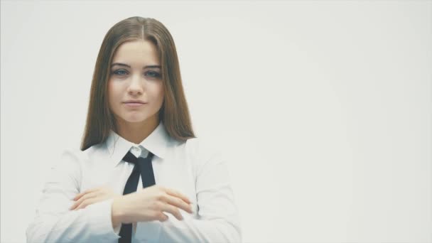 Young girl smiling standing on a white background. During this time, a call to the class shows a gesture and puts a hand on hand. — Stock Video