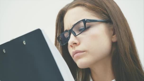 Close-up La mujer de negocios se levanta sobre un fondo blanco. Sin embargo, contiene una carpeta negra con documentos y los lee cuidadosamente. . — Vídeos de Stock