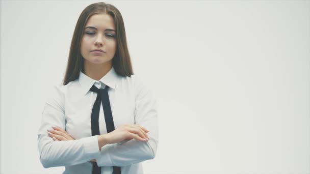 Zeker een jonge vrouw van Europese normen. Het dragen van een wit overhemd kijkt zorgvuldig in de camera. Geïsoleerd op een witte achtergrond. Het zetten van een hand op zijn hand glimlacht. — Stockvideo