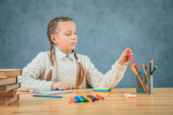 Школьница сидит за столом и выбирает цветной карандаш . — стоковое фото