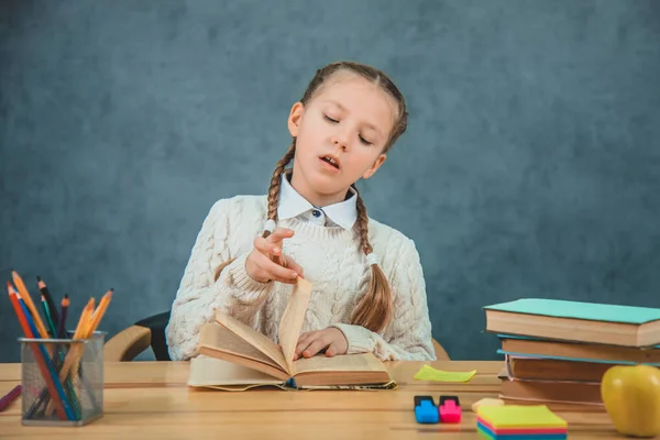 Hübsche junge Schülerin mit blonden Haaren, die aus einem Buch lugt und desinteressiert draufschaut, isoliert auf dem grauen Hintergrund — Stockfoto