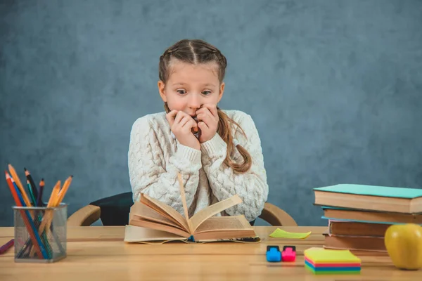 Porträtt av Young bedövade förvånad chockad elev flicka med en bok vid skrivbordet. — Stockfoto