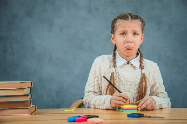 Verdrietig kleine dame zit aan de balie waarop zijn stickers, schaar, markeerstiften, en een stapel boeken. — Stockfoto