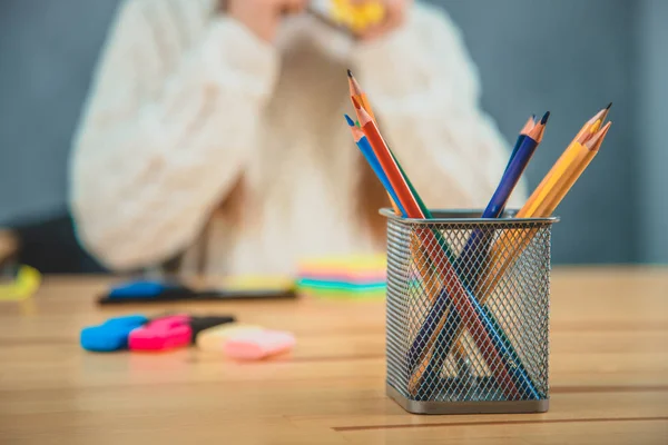 Fundo desfocado, onde a estudante está sentada com as mãos no ar. Pilha de lápis de diferentes cores está em primeiro plano . — Fotografia de Stock