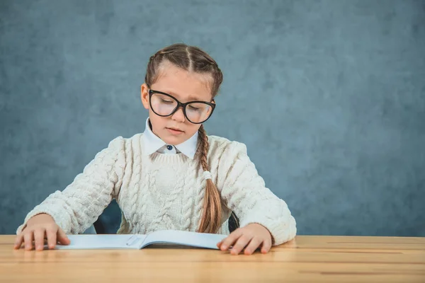 Portrait of lovely light haired schoolgirl looks attentively at the copybook, poses on the grey background. — Stock Photo, Image