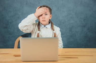 Sevimli küçük büyüleyici sarışın kız ön bir laptop oturuyor. Kız ödevini unutmuş ve kafasını sağ eliyle dokunuyor..
