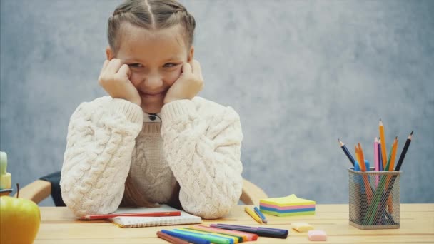 Biraz yorgun ama yine de gülümseyen okul çocuğu masanın üzerine dirseklerini koyarak ve yüzünü elleriyle tutarken — Stok video