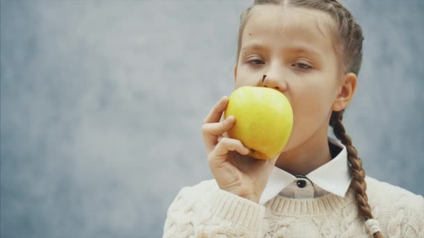 Pequeño escolar está comiendo una gran manzana amarilla . — Vídeos de Stock