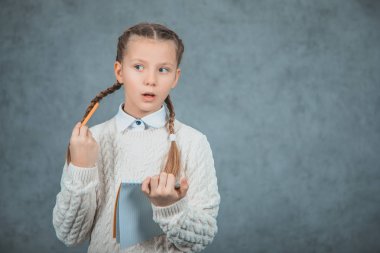 Sevimli bir kız öğrenci güzel giysiler onu örgüleri ile oynarken gri backgriunds izole olduğunu.