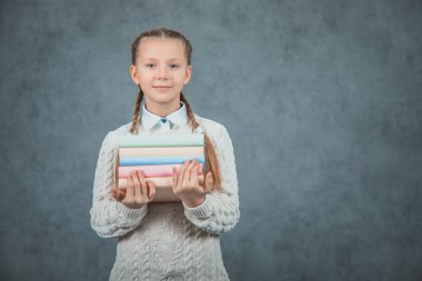 Gri arka planlar üzerinde izole edilmiş kitaplarını kucaklayan akıllı bir kızın yakın çekim portresi.