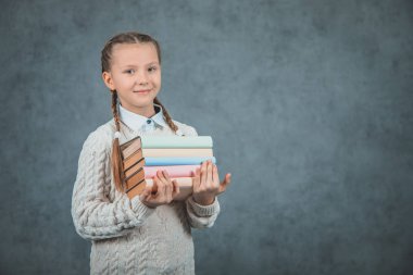 Gri arka planlar üzerinde izole edilmiş kitaplarını kucaklayan akıllı bir kızın yakın çekim portresi.