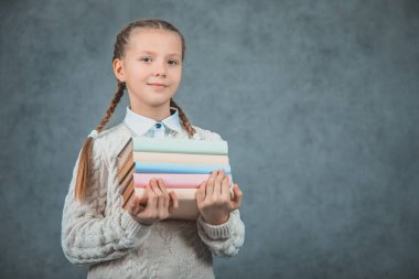 Gri arka planlar üzerinde izole edilmiş kitaplarını kucaklayan akıllı bir kızın yakın çekim portresi.