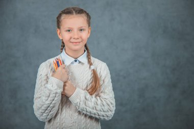 Birinci sınıf öğrencisi gri arka planda renkli kalemler tutan