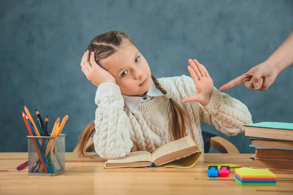 Uttråkad cuteschoolgirl vägrar att läsa titta på kameran sitter vid skrivbordet. — Stockfoto