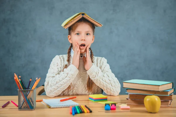 Suprised schoolgirl is with an open book on her head watching with an amusement and wonder. Good student and a quich learner is ready to study. — Stock Photo, Image