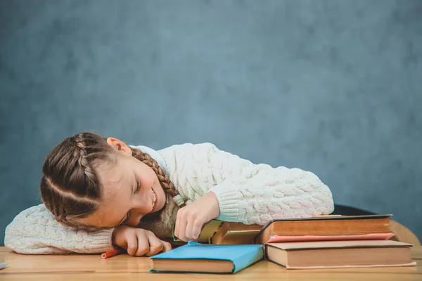 Tired, but happy schoolgirl is lying down the books, which are on the desk. Photo of little schoolgirl, who is smiling to an education. — Stock Photo, Image