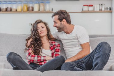 Genç çift kendilerini zevk ve oturma odasında kanepede tv izlerken geri görünümü. Genç adam ve kadın rahatlatıcı ve yeni düz kırmızı şarap içme.