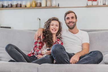 Güzel bir kız ve genç bir adam kanepede oturan ve Tv izlemek. İnsanlar kanepede rahatlar. Gözlüklü ve mavi gömlekli genç bir adam. Gözlüklü genç kadın.