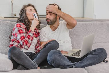 Evde bir kanepede otururken bir dizüstü bilgisayar kullanarak ve gülümseyerek online alışveriş yaparken iyi bir çift.
