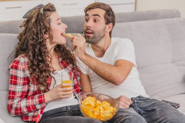 Gülümseyen eş ve adam kanepede oturuyor. Bu izle tv sırasında. Birbirlerine cips verin.