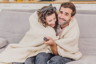 Genç çift kendi dairede rahatlatıcı, kanepede oturan, Tv izlerken. Bir battaniye ile kaplı, mutlu sarılma.