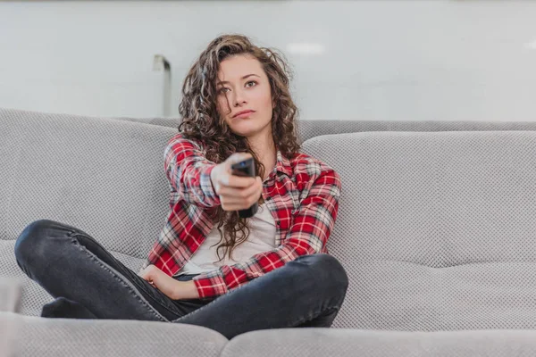 The young spectator wife watches the TV at home. During this time, sitting on the couch in the living room. — Stock Photo, Image