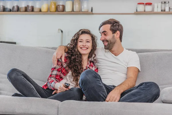 Menina bonita e um jovem sentado no sofá e assistir TV. As pessoas relaxam no sofá. Jovem de óculos e camisa azul. Jovem com óculos. . — Fotografia de Stock